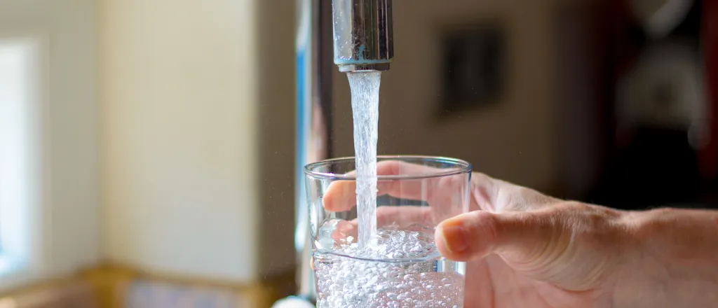 Hand filling a glass with water from a faucet.