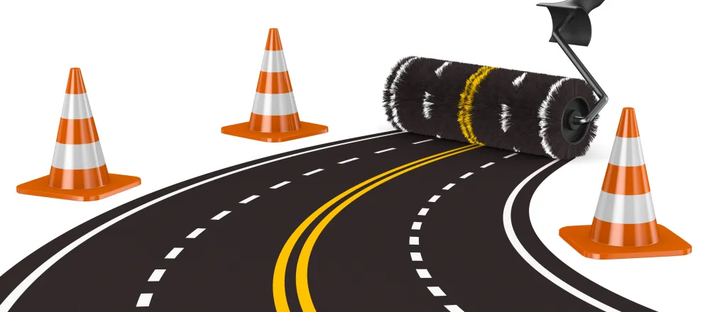 Concept image of a paint roller creating a four-lane road. Construction cones are at the sides.