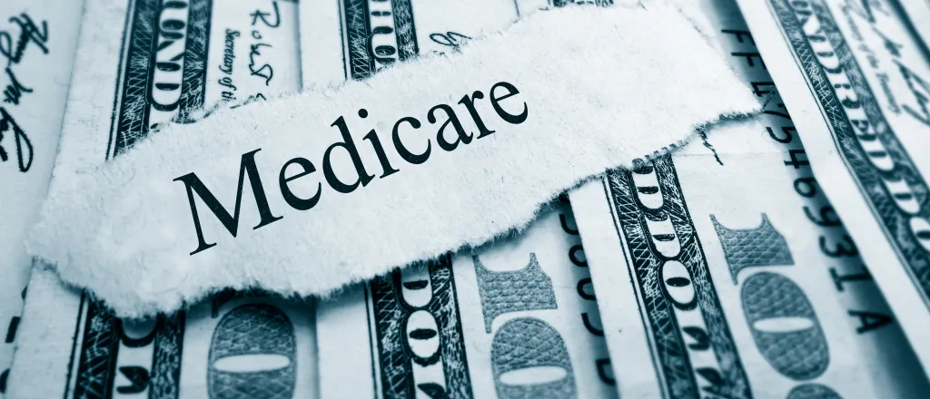 A scrap of torn paper with the word "Medicare" rests on top of a spread of United States 100 dollar currency.