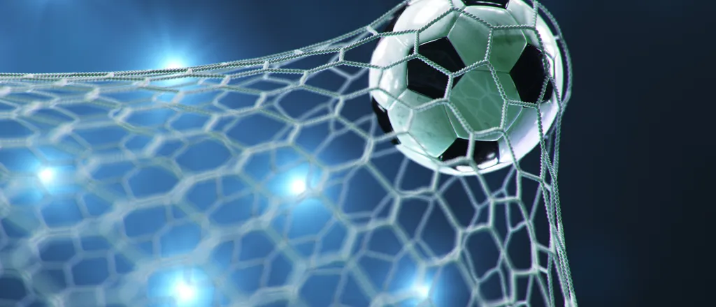 Soccer ball/football stretching the goal net with stadium lights in the background.