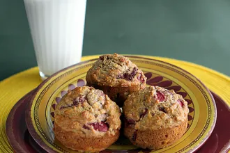 Stack of two plates on a placemat with three Banana Berry Muffins next to a glass of milk.