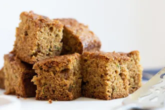 Stack of cut pineapple zucchini cake squares. A serving spatula is blurred in the foreground.