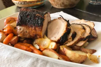 Serving plate with a partially sliced pork loin roast along side cook carrots and potatoes.