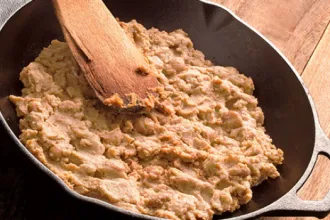 Cast iron pan containing refried beans. An old wooden spoon rests on top of the beans.