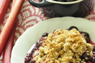 Bowl of Rhubarb Blueberry Crisp next to a cup.