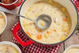 Overhead view of a pot of cheese and corn chowder. Smaller bowls of chowder are nearby.